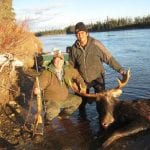 2 friends posing with a bull moose