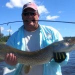 Man holding a pike with a fishing rod in his mouth